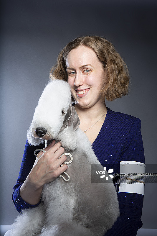 在工作室里被微笑的主人抱着的贝灵顿梗犬图片素材