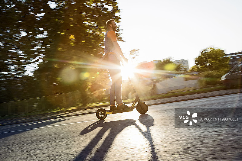在城市道路上逆着夕阳骑滑板车的潮男图片素材
