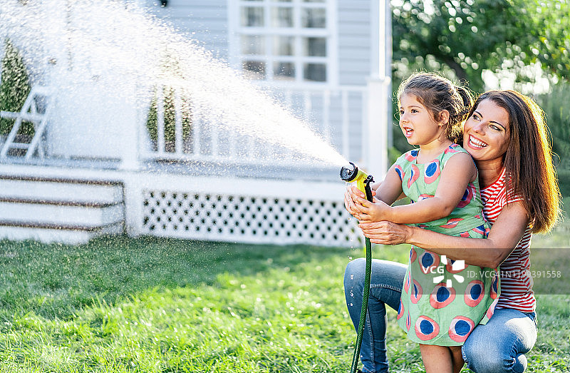 母亲在后院泼水和女儿玩耍图片素材