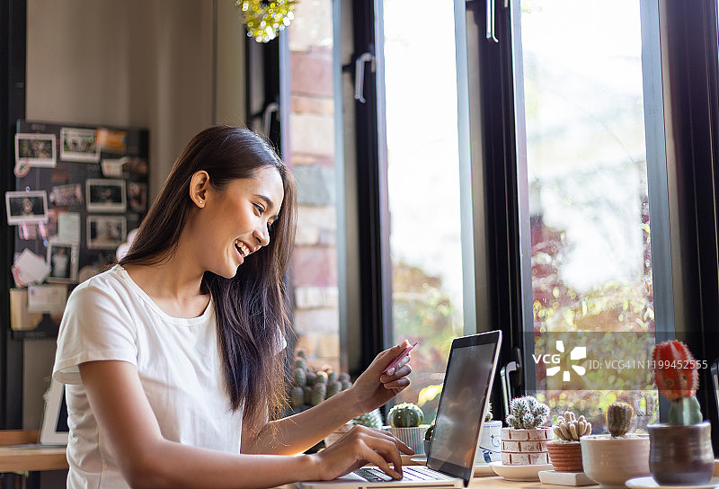 亚洲女性在咖啡馆用信用卡和笔记本电脑网购图片素材