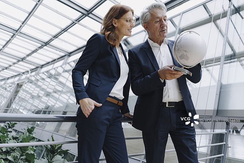 在现代办公楼里看地球仪的商人和商人图片素材