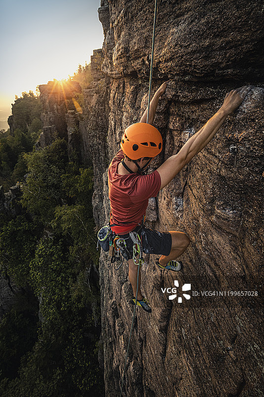 男子在德国巴登-巴登的巴特岩石上攀爬，日落时分图片素材