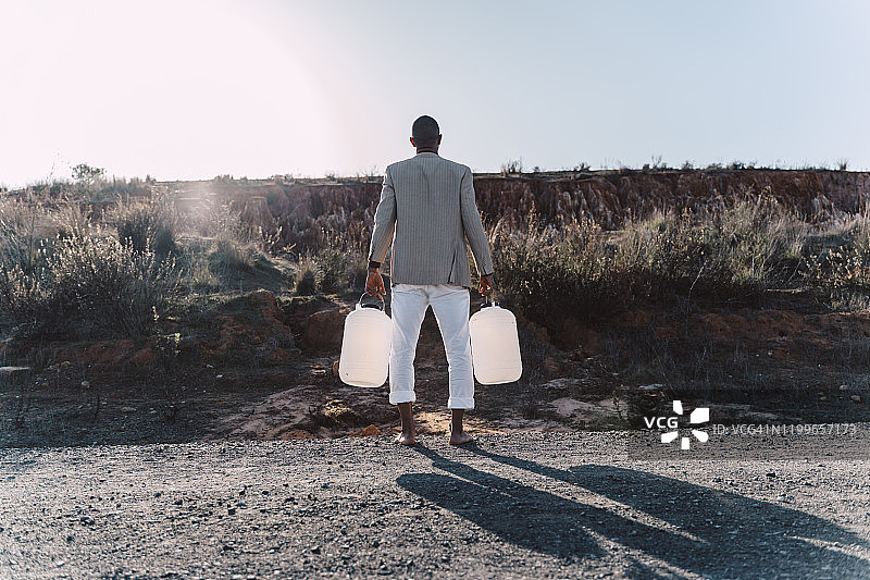 站在土路上，手持空水罐的年轻男人图片素材