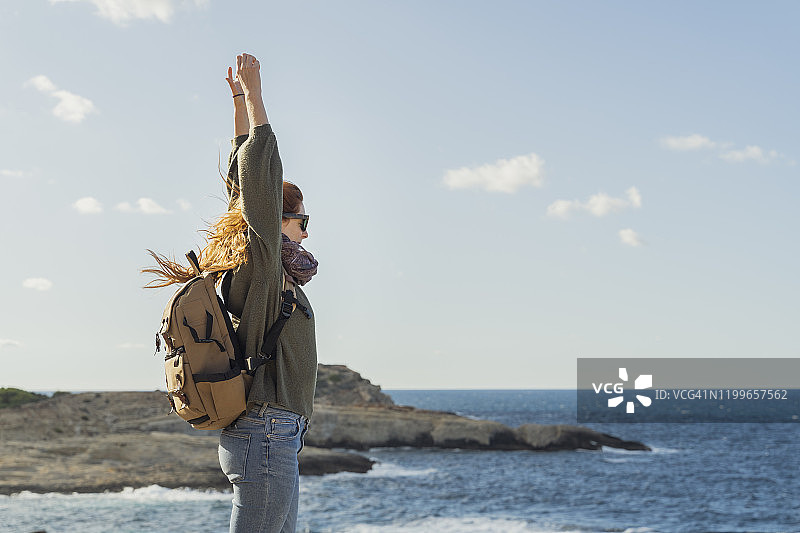 西班牙伊比萨岛海边举起双臂的红发年轻女子图片素材