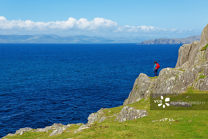 年轻女子在爱尔兰比拉半岛羊头悬崖上，背着红色背包的背影图片素材