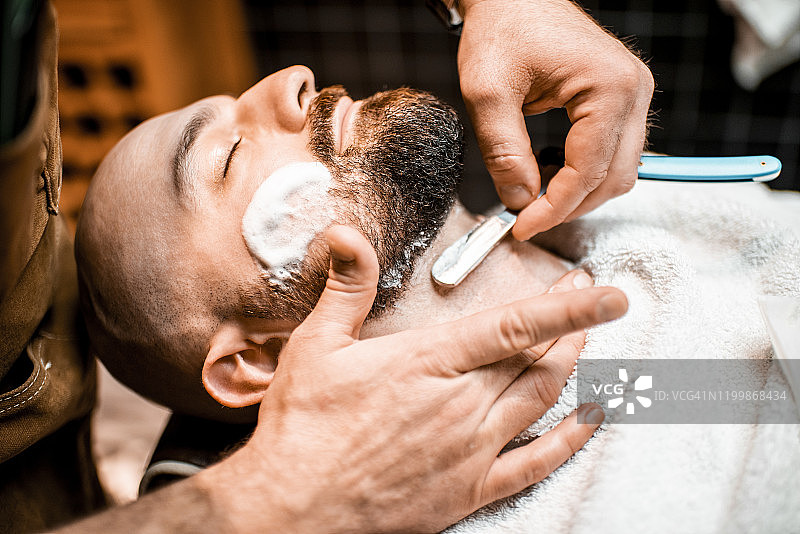 在理发店里，年轻的络腮胡男子用剃须刀修饰胡须图片素材