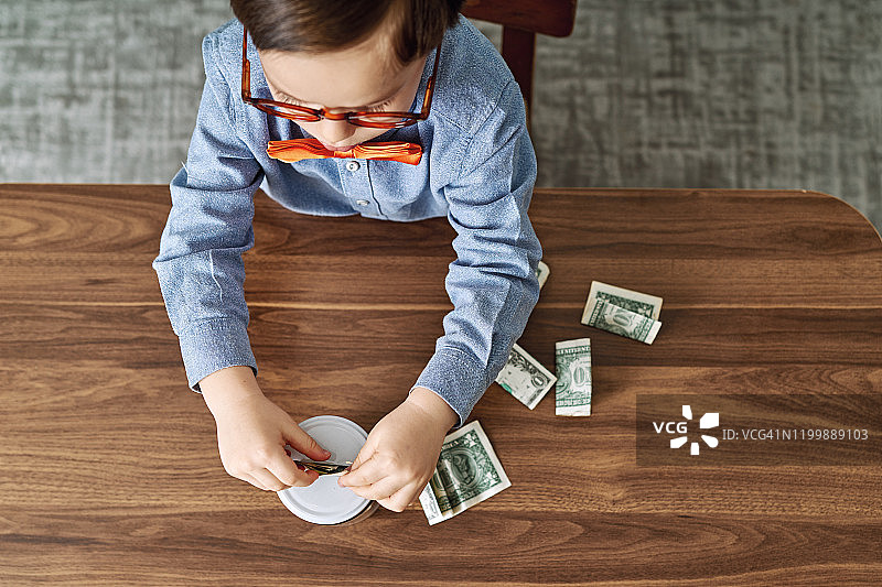 将钱存在玻璃罐里，为未来储蓄的可爱儿童图片素材