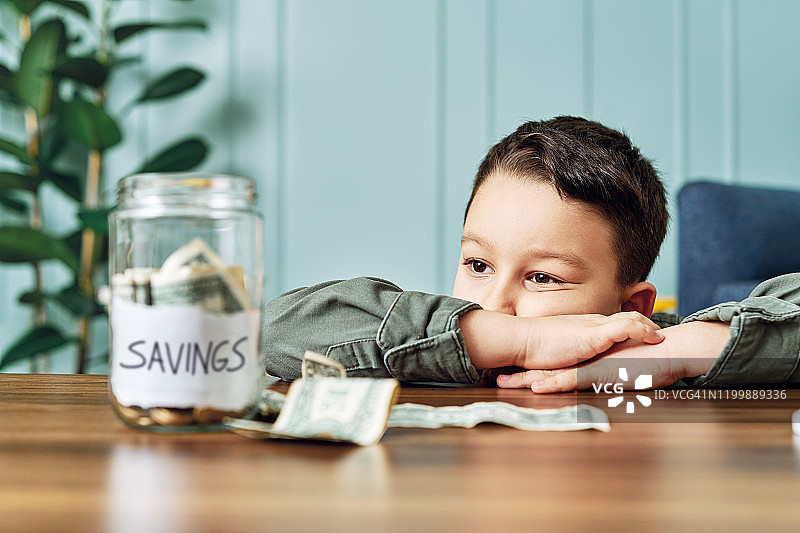 将钱存在玻璃罐里，为未来储蓄的可爱儿童图片素材
