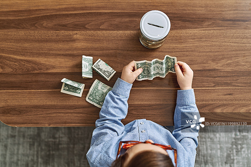 将钱存在玻璃罐里，为未来储蓄的可爱儿童图片素材