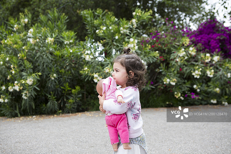 小女孩在私人道路上抱着洋娃娃的侧影图片素材