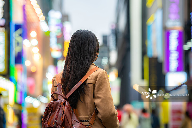 亚洲女性在韩国首尔明洞购物街的灯光下行走。图片素材