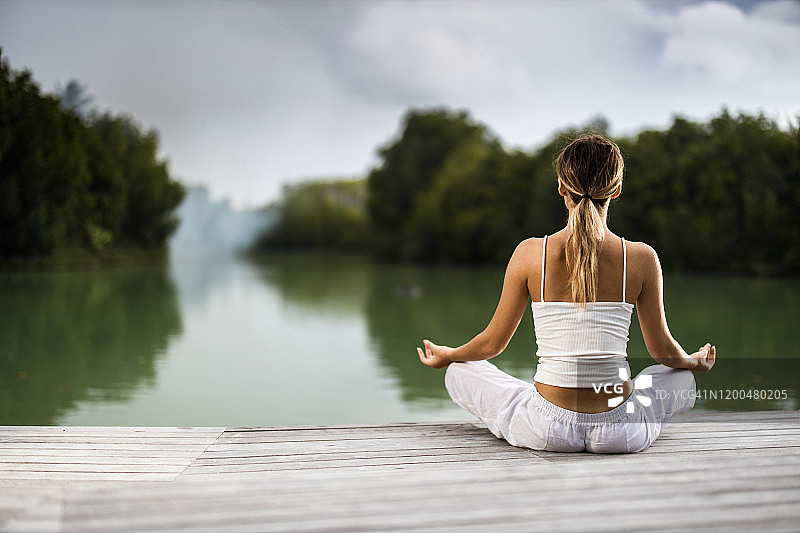 在河边码头上以莲花姿势练习瑜伽的女子背影图片素材