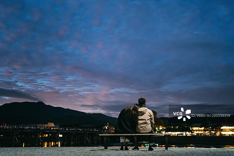 日落时分，在京都东山传统日式小镇湖边长椅上欣赏美景的情侣背影图片素材
