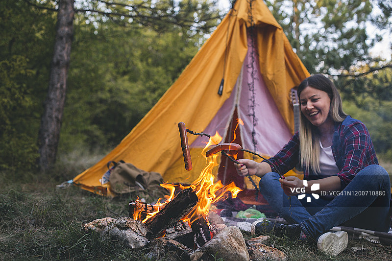 露营：快乐的女人在篝火旁准备美味香肠图片素材