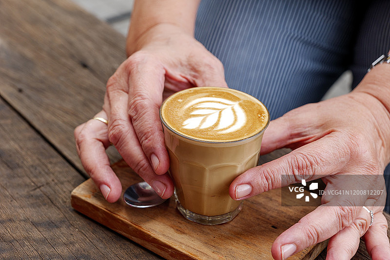 焦点选择：手持卡布奇诺或拿铁，木质托盘与桌面，复古风图片素材
