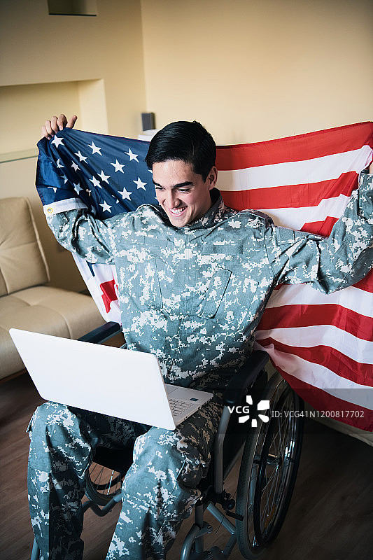 使用笔记本电脑并手持美国国旗的退伍伤残士兵图片素材