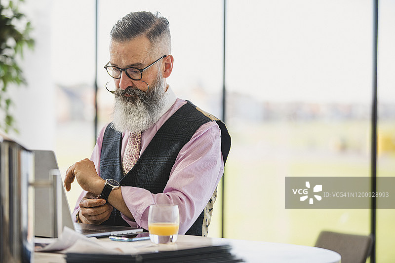 时髦商务人士查看手表，使用笔记本电脑图片素材