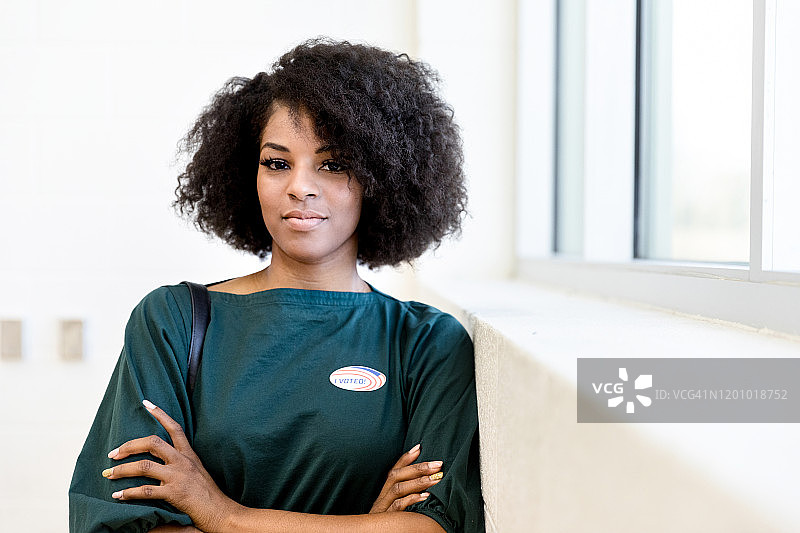 一位手臂交叉、贴着投票贴纸的女人靠在墙上图片素材