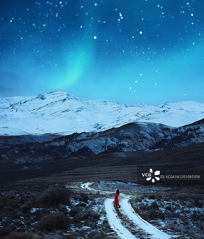 雪山山谷中，红衣女子走在雪地小路上，背景是北极光图片素材