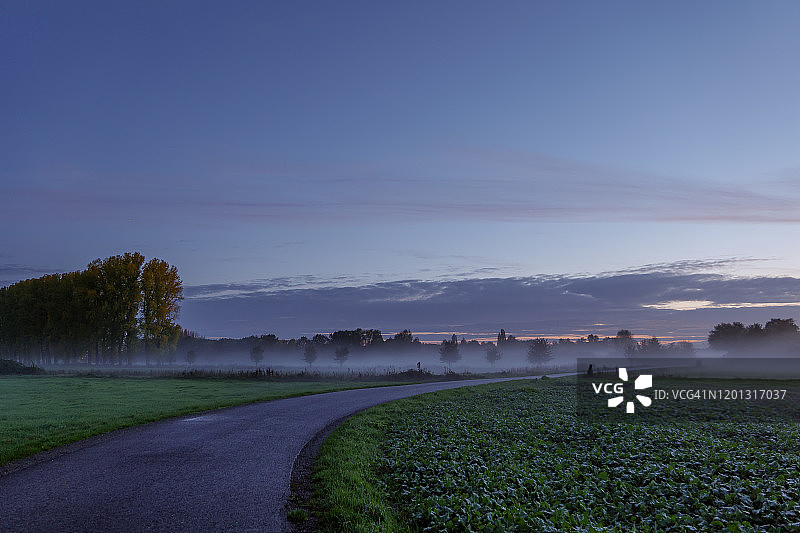 宁静的乡村公路日落，农田之间，蓝金色暮光天空，薄雾缭绕图片素材