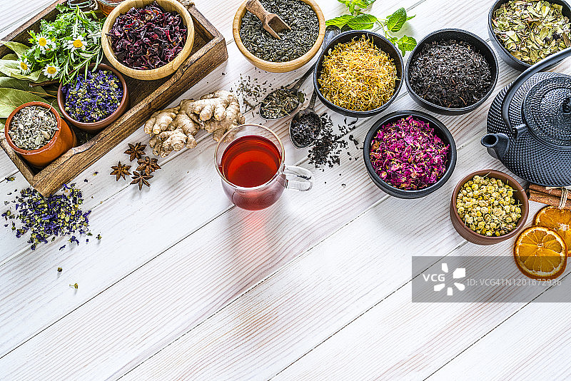 白色桌子上方拍摄的各种彩色干茶叶和花朵，留白图片素材