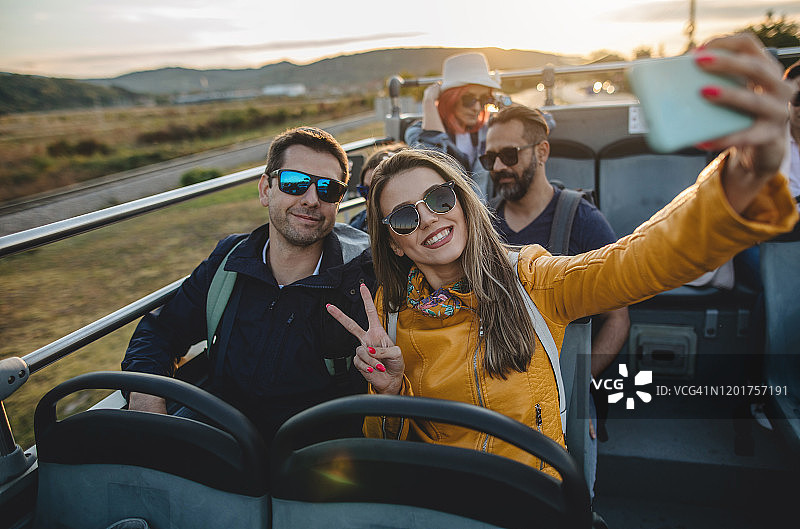 快乐的年轻情侣在露天巴士上用手机自拍图片素材