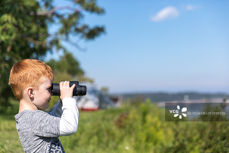 夏天露营时用双筒望远镜观鲸的红发小男孩图片素材
