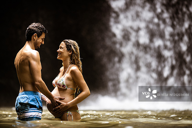 快乐的孕妇夫妇在雨林的水中交谈图片素材