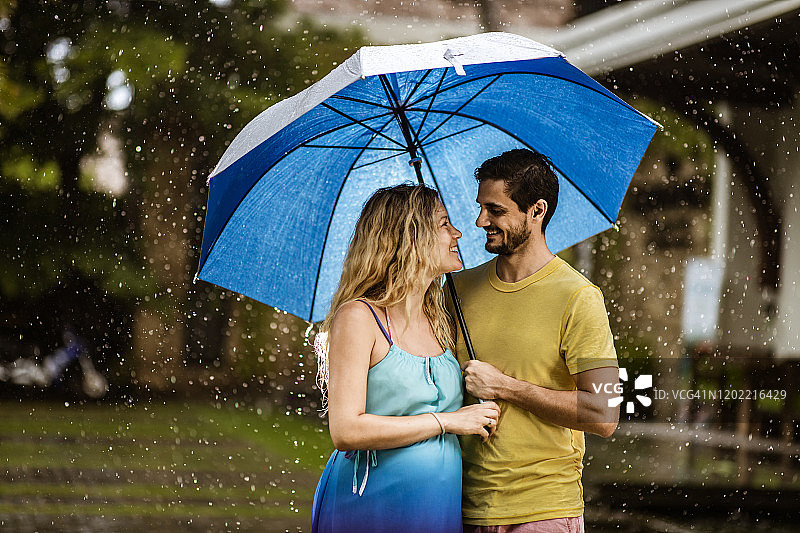 快乐的孕妇夫妇在雨天在伞下交谈图片素材
