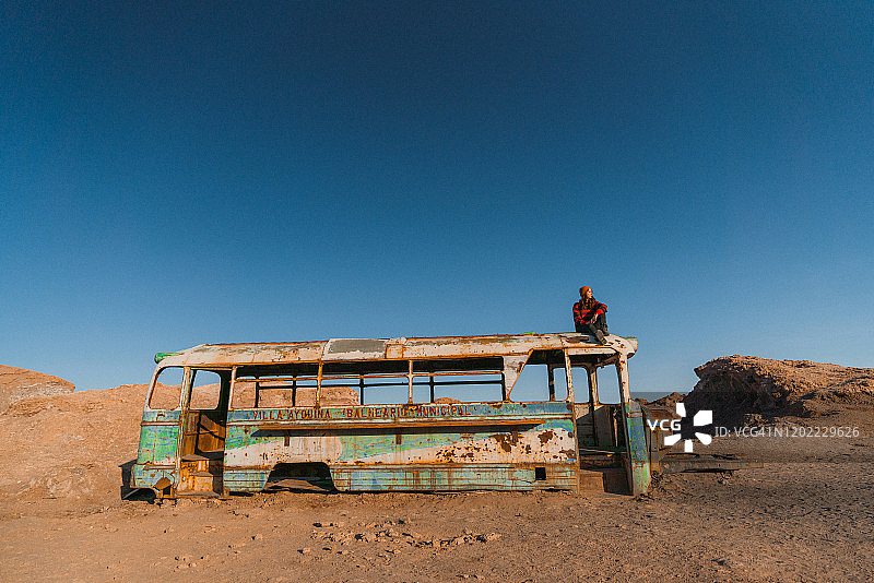 坐在阿塔卡马沙漠废弃巴士顶上的女人图片素材