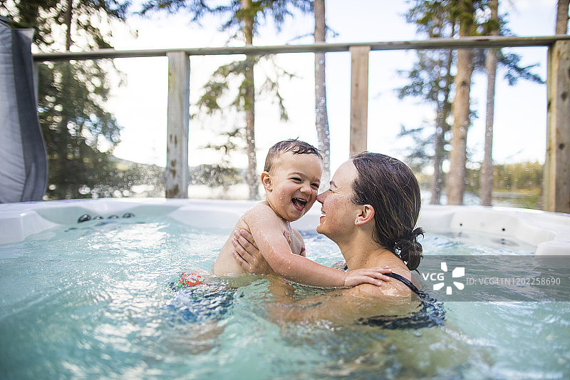 小男孩在游泳池里和母亲一起玩水花图片素材