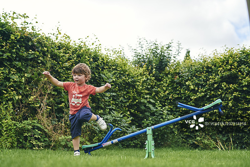 男孩在花园里跳下玩具跷跷板图片素材