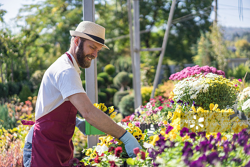 快乐的年轻园丁检查开花植物图片素材