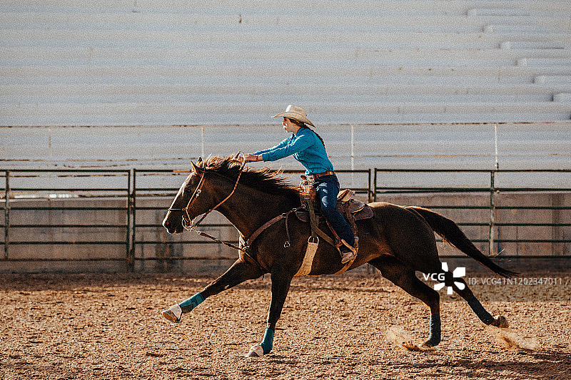 在竞技场上，一位十几岁的牛仔女郎让她的马加速参加绕桶比赛。图片素材