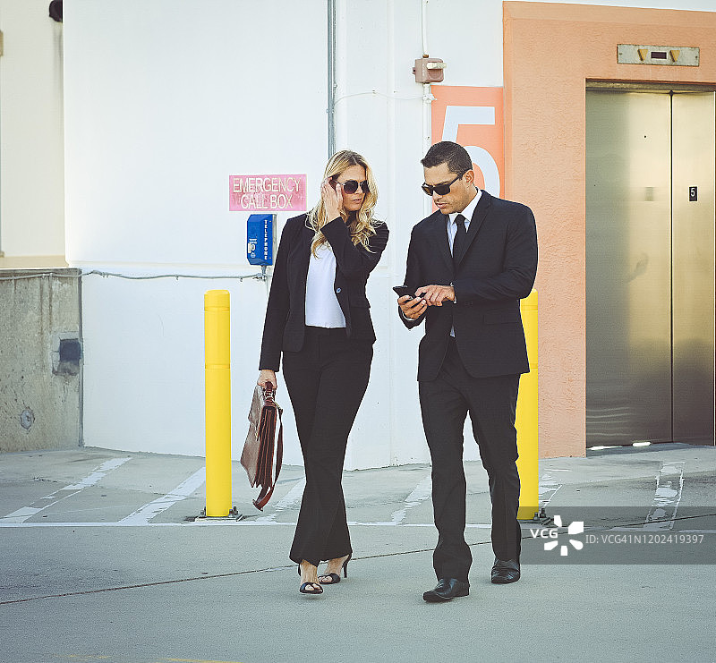 穿着商务装和太阳镜在户外行走的企业商务同事图片素材