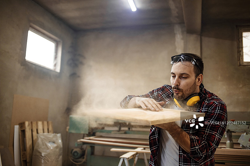 年轻英俊的木匠吹掉锯末的照片图片素材