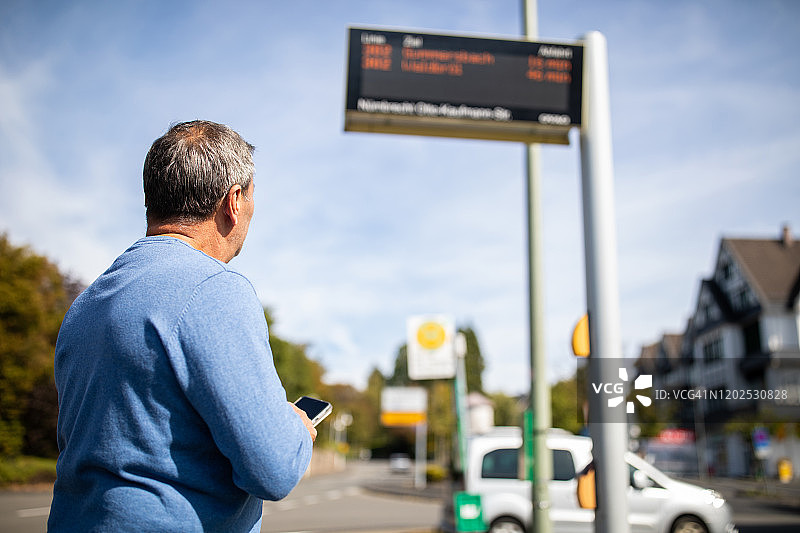年长的男人站在那里查看公共汽车到站信息系统图片素材