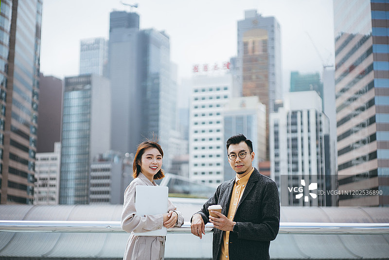 年轻的商务伙伴在城市阳台上合作处理商业项目，背景是现代办公楼图片素材