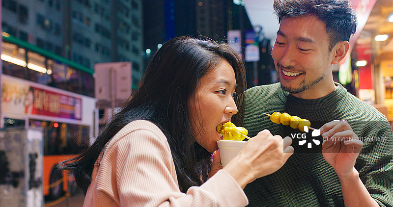 年轻情侣在夜晚一起享用街头小吃图片素材