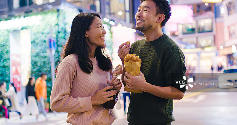 年轻情侣在户外夜市品尝鸡蛋仔和珍珠奶茶图片素材