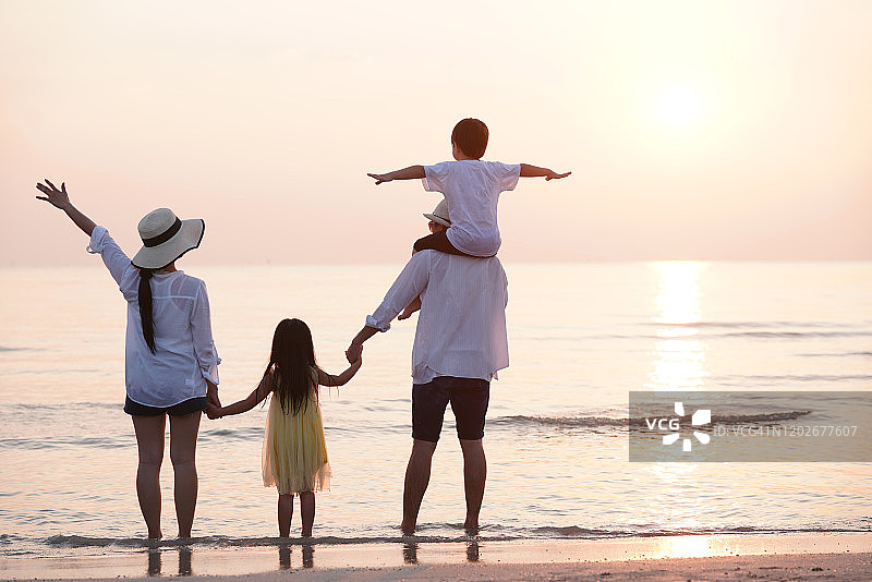 一家人站在海滩上欣赏日落背景的背影图片素材