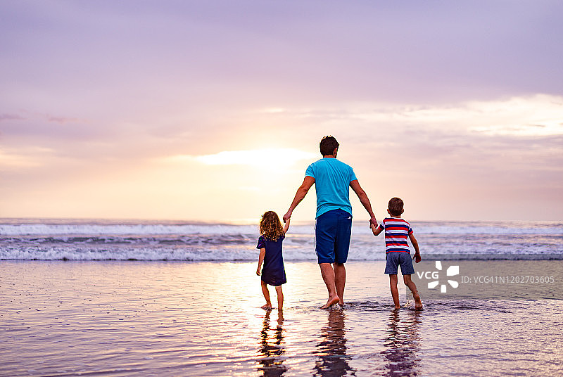 单身父亲和孩子们在黄昏时分在海滩上奔跑的背影图片素材