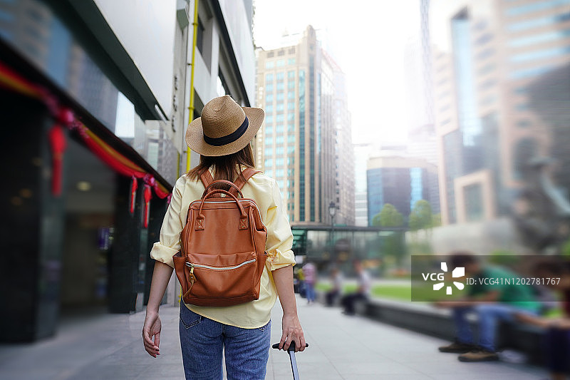 年轻女子背着背包和帽子前往新加坡市中心的背影。新加坡旅行概念。图片素材