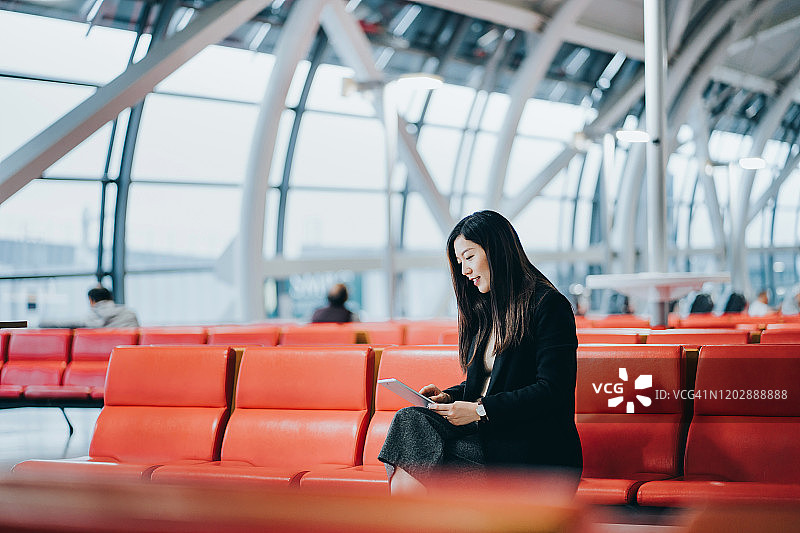 在机场休息室用平板电脑阅读的年轻亚洲女性图片素材