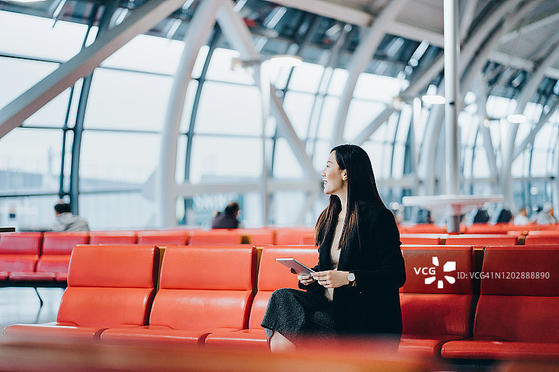 在机场休息室用平板电脑阅读的年轻亚洲女性图片素材