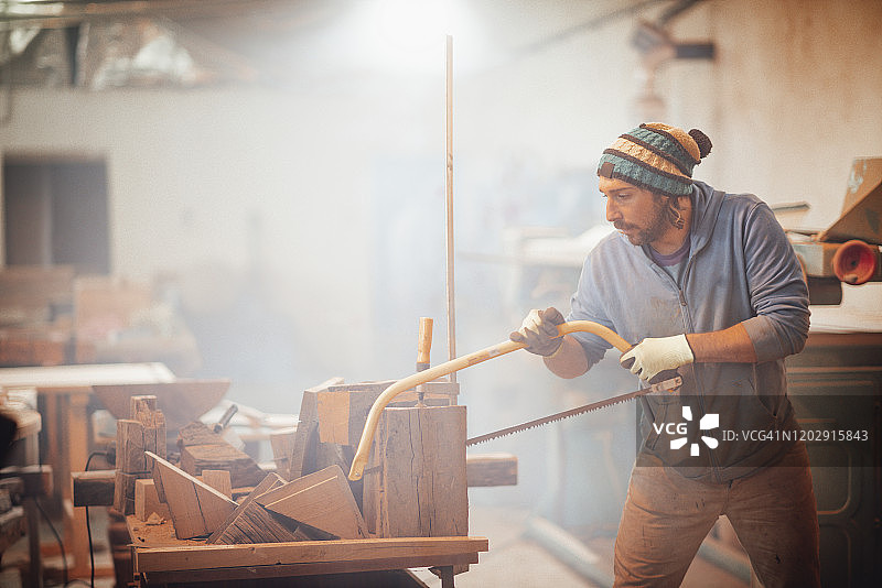 年轻木匠用弓锯在工作台上锯木头图片素材