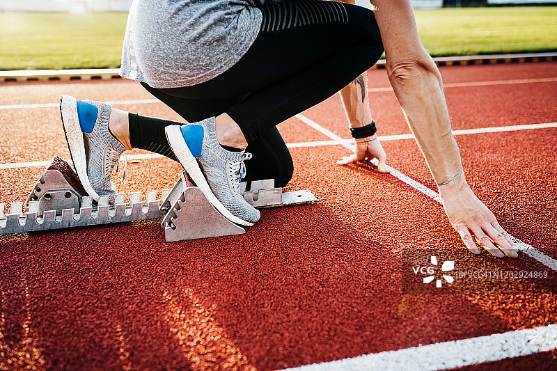 女人蹲在室外跑道起跑器上的特写图片素材