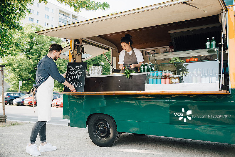 男店主在小吃摊上调整木板，合伙人在餐车里工作图片素材
