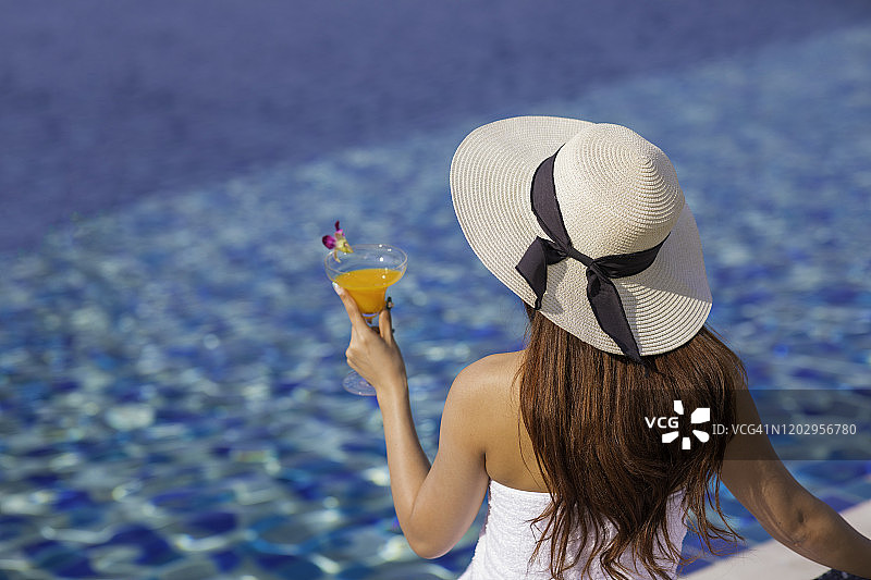 女孩在泳池边放松，喝着新鲜果汁图片素材