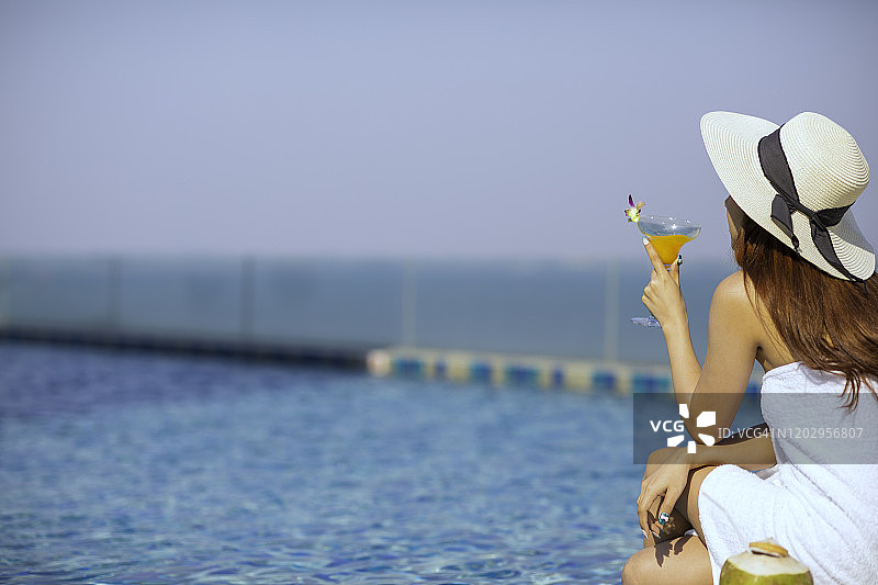 女孩在泳池边放松，喝着新鲜果汁图片素材